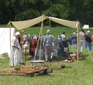 A woman in period garb tends a fire in the encampment.